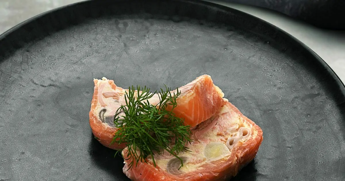 Salmon roulade with dill on a dark plate.