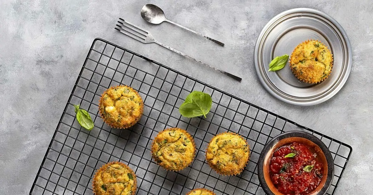 Savory spinach muffins with a side of tomato sauce, fork, and spoon on a cooling rack.