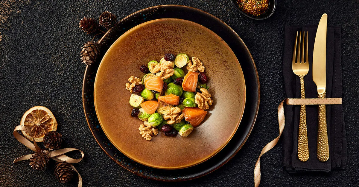 Salmon and Brussels sprout salad with walnuts and cranberries, served on a rustic plate with festive decorations.