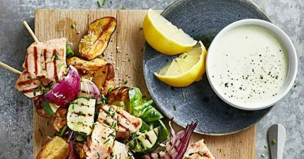 Grilled salmon skewers with roasted potatoes, red onion, zucchini, and lemon wedges served with dipping sauce.