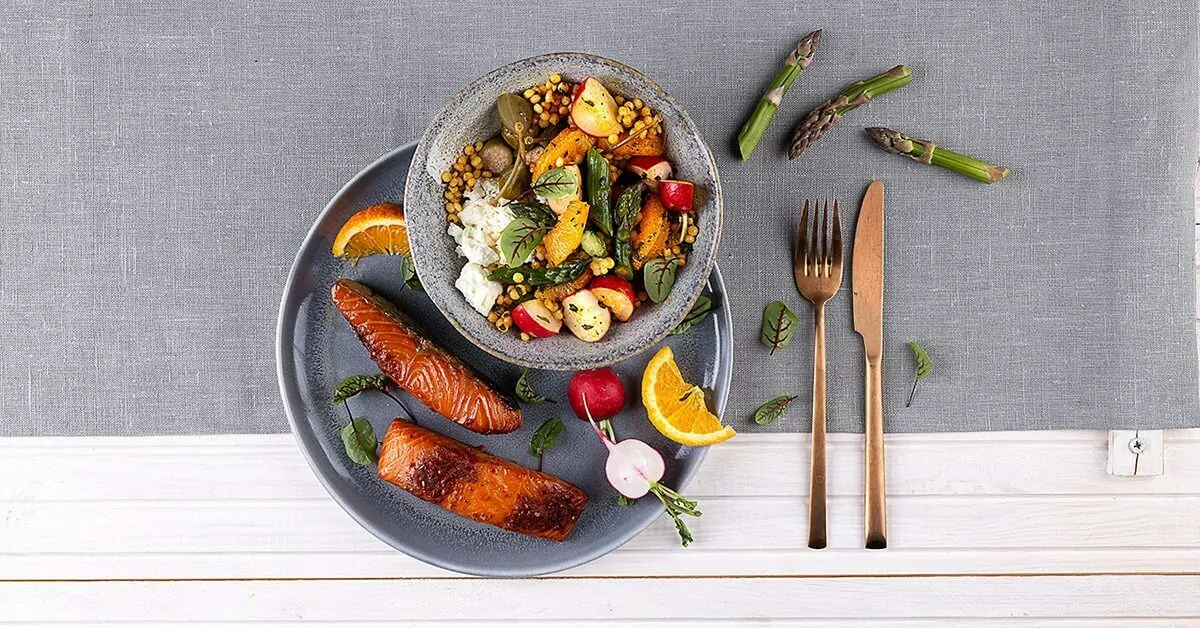 Salmon with couscous salad, asparagus, and orange slices, set with copper cutlery.