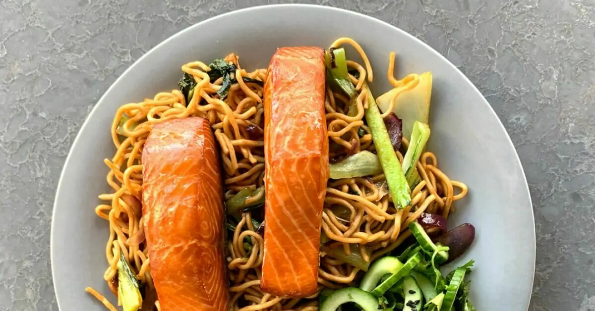 Two salmon fillets atop a bowl of noodles and vegetables.