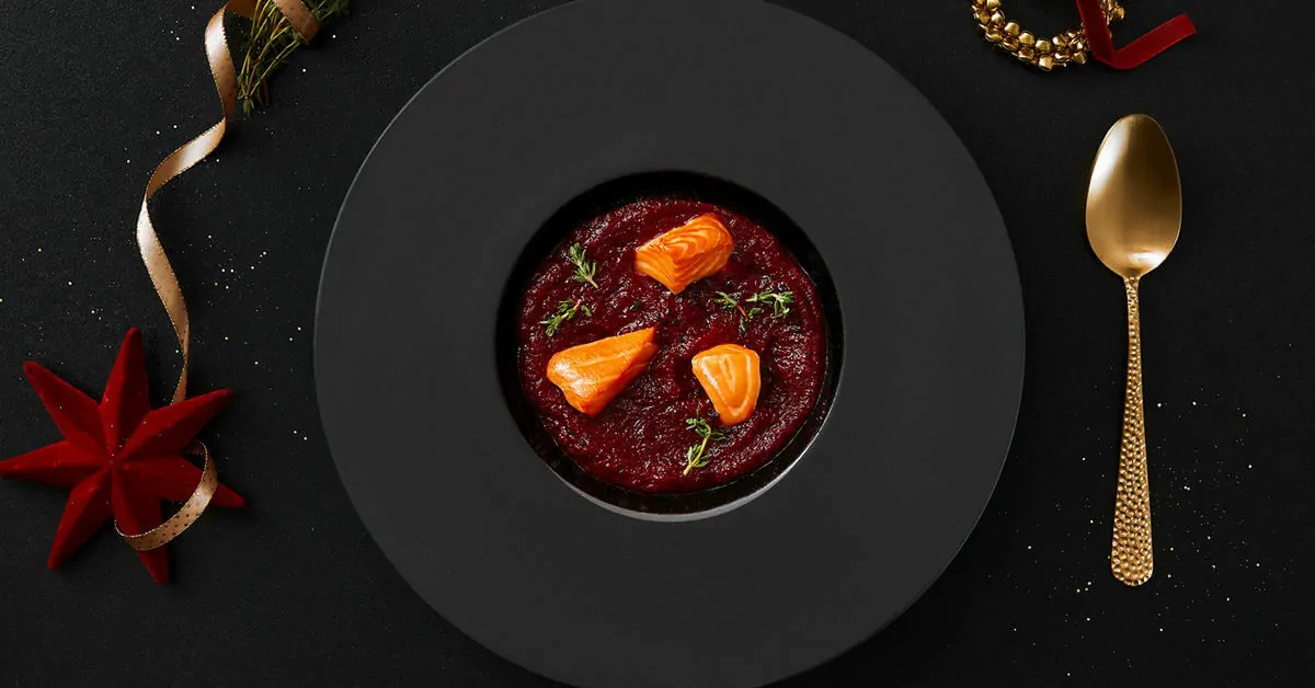 A festive dish of beet soup with salmon and herbs, served with a golden spoon.