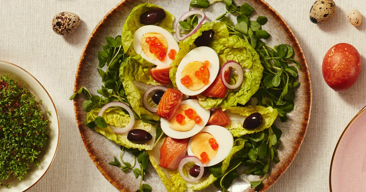 A salad with eggs, salmon, olives, and red onion, with speckled eggs and a red egg nearby.