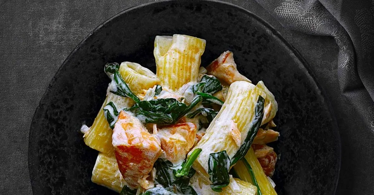 Creamy pasta with salmon and spinach in a black bowl.